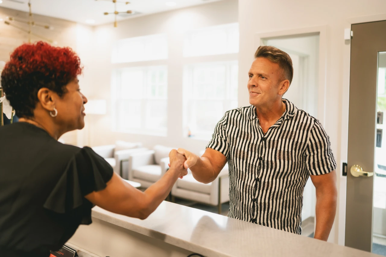 Male dental patient smiling and shaking hands with the receptionist at The Dental Wellness Company.